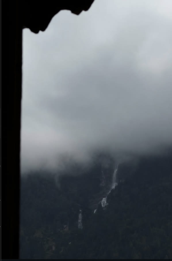 A mist-covered mountain and distant waterfall seen through a dark window