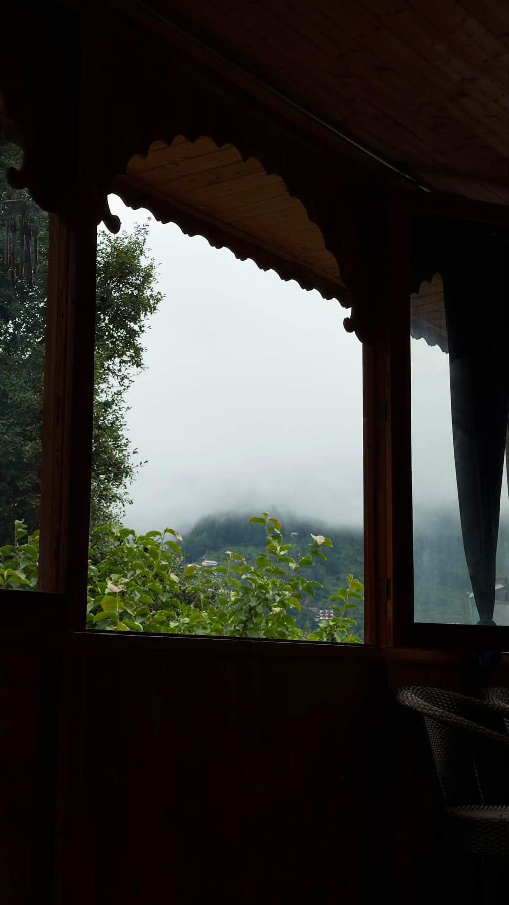 Carved wooden balcony window looking onto mist and green hills