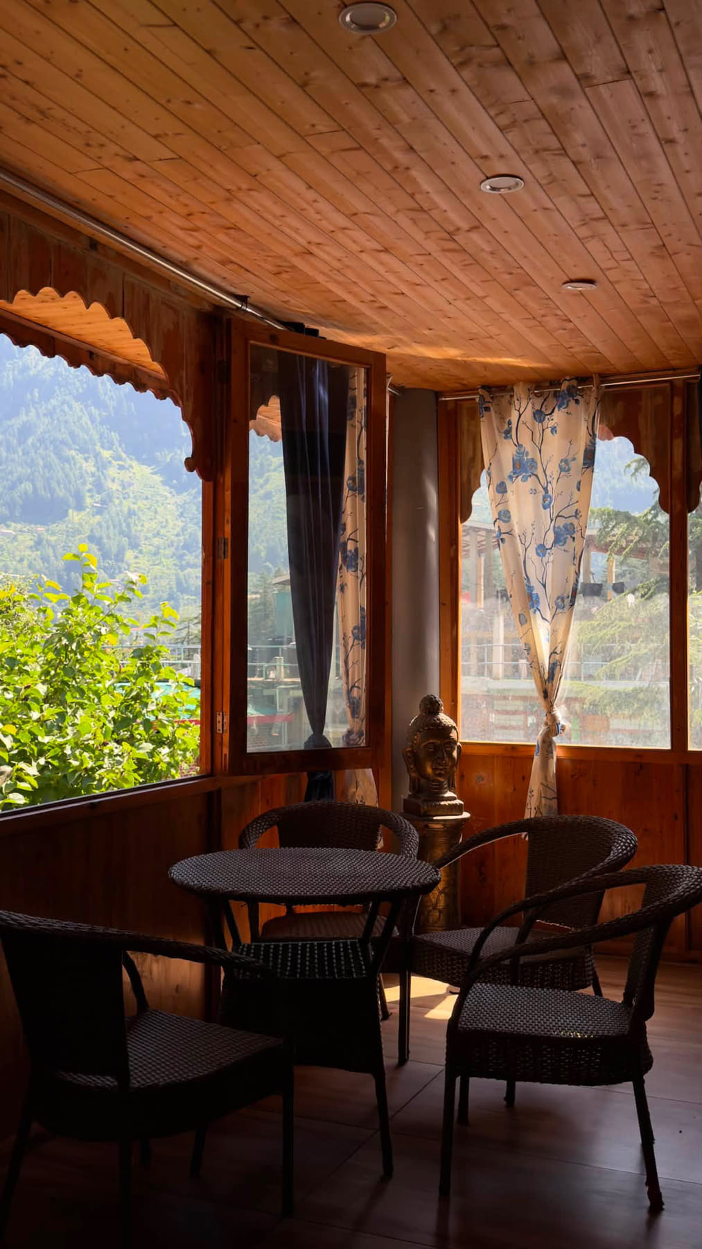 Sunlit wooden balcony with wicker chairs, a small table and mountain views