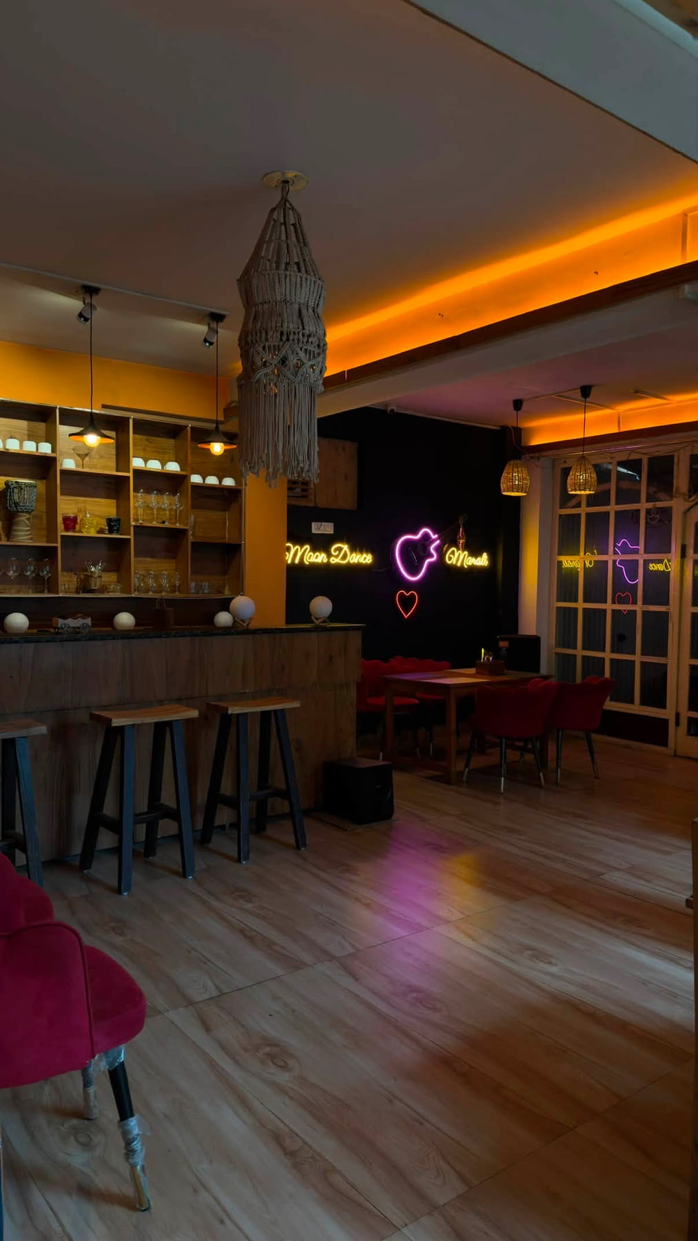 Café bar with neon Moon Dance Manali signs, wooden stools and red chairs