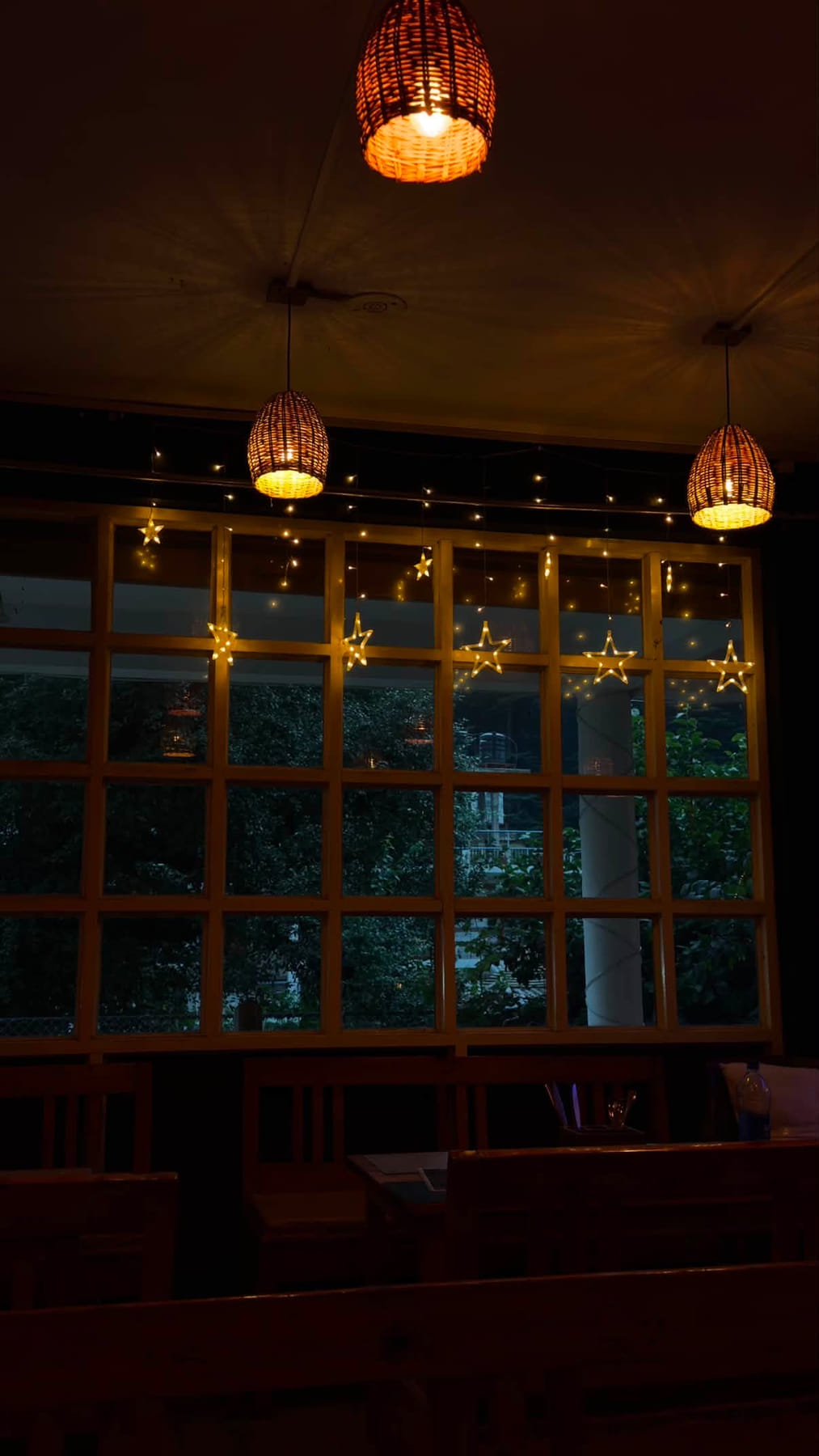 Café window at night with woven lamps and hanging star lights over dark trees
