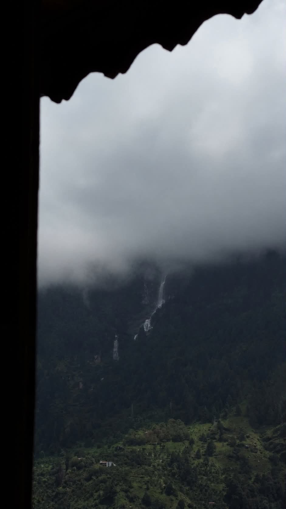 Waterfalls on a forested mountain seen through a dark carved eave