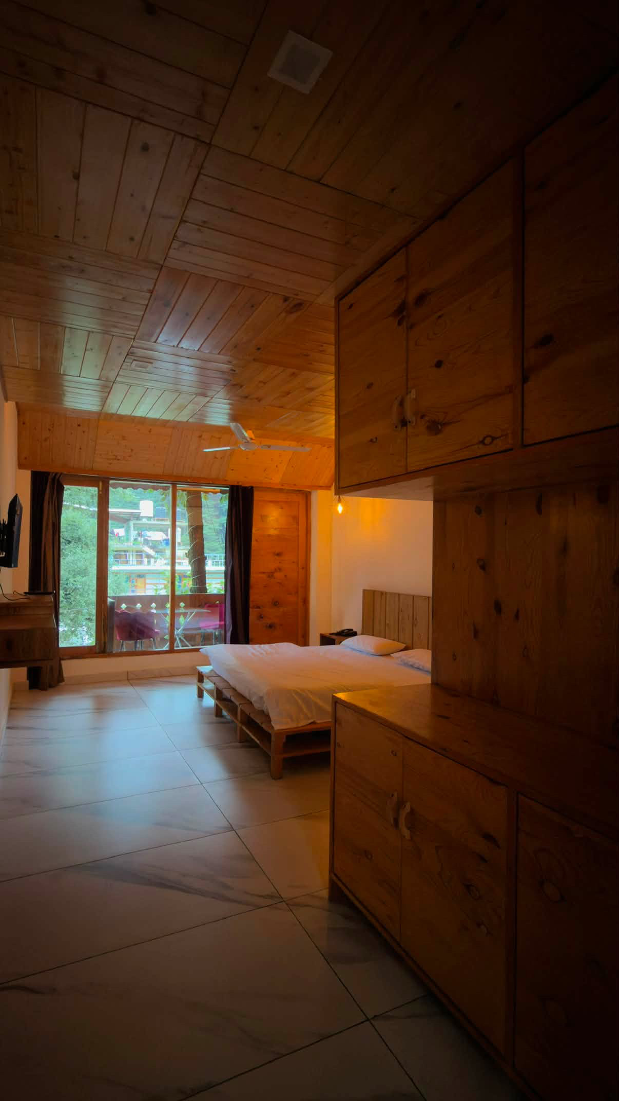 Wood-panelled hotel room with double bed, wardrobe, television and balcony in Old Manali